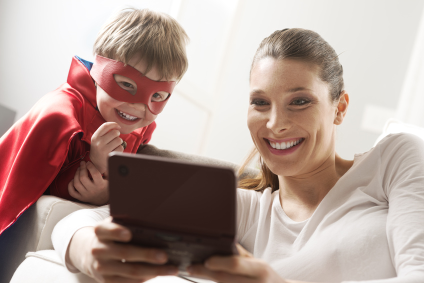 Medienkompetenz: Mutter spielt mit ihrem als Superheld verkleideten Sohn Videospiele